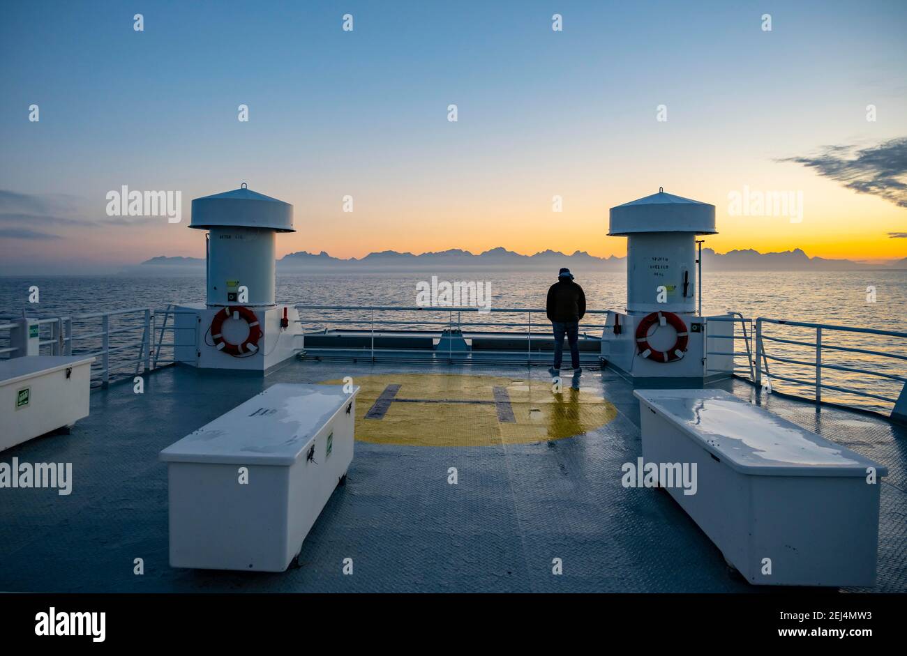 Passenger looking over the ocean, evening mood on ferry in front of silhouette of mountains, Lofoten, Nordland, Norway Stock Photo