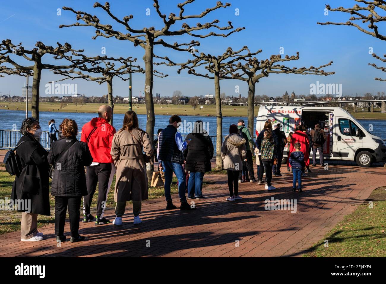 Düsseldorf, NRW, 2021. A long queue has formed in front of an ice cream van. People enjoy their Sunday afternoon in beautiful warm sunshine with temperatures up to 18 degrees in the popular MedienHafen (media harbour) district, a redeveloped area by the river Rhine hosting media companies, offices, entertainment, restaurants and leisure facilities in Düsseldorf, the capital of Germany's most populous state of North Rhine-Westphalia. Credit: Imageplotter/Alamy Live News Stock Photo