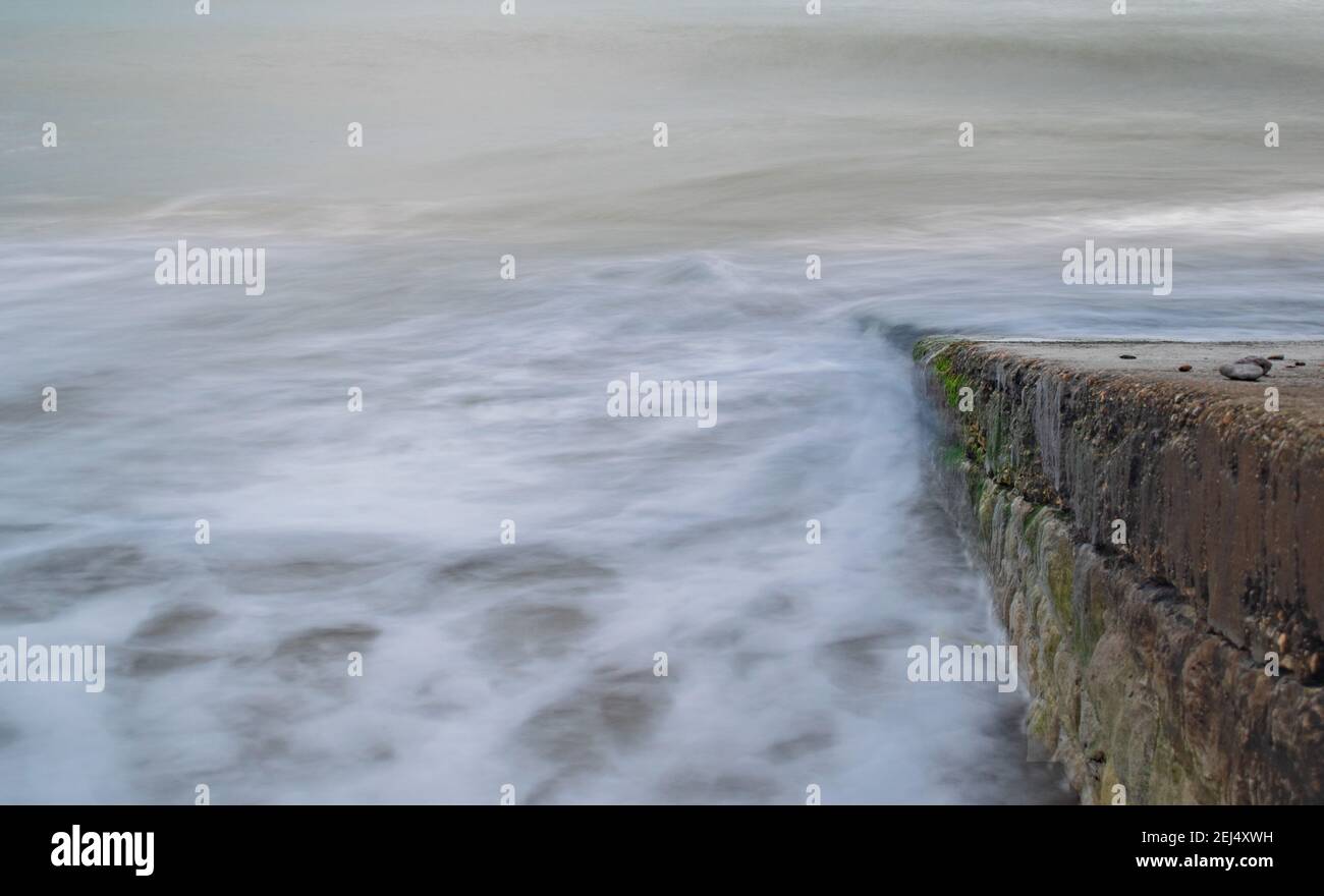 The milky foamy water blurs into the sky in slow motion as it rolls down a slipway into the ghostly sea at Swanage Bat, Dorset England Stock Photo