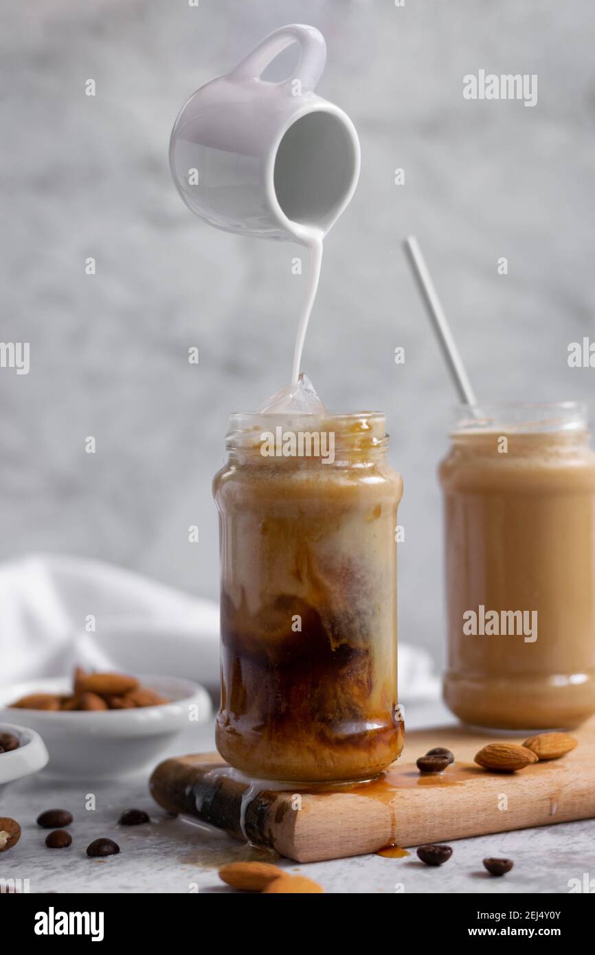 Levitating jar pouring almond milk over iced coffee,  refreshing energizing drink Stock Photo