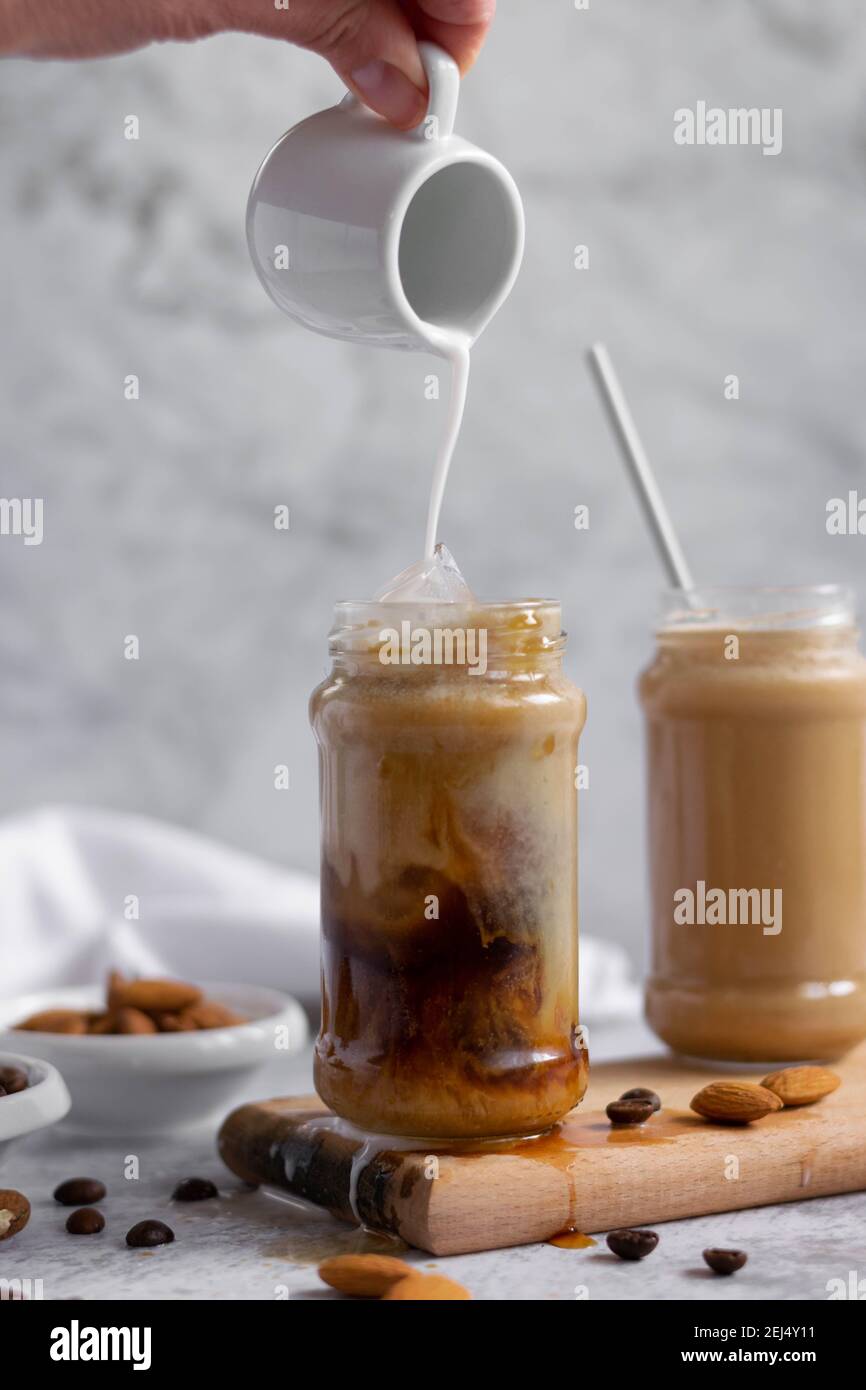 Pouring almond milk over iced coffee, refreshing energizing drink Stock Photo