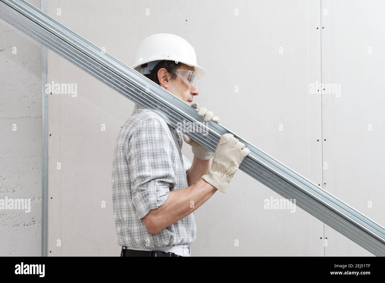 man worker with drywall metal profiles for installing plasterboard sheet to wall. Wearing white hardhat, work gloves and safety glasses. Isolated on w Stock Photo