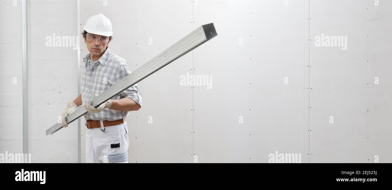 man worker with drywall metal profile for installing plasterboard sheet to wall. Wearing white hardhat, work gloves and safety glasses. Isolated on wh Stock Photo