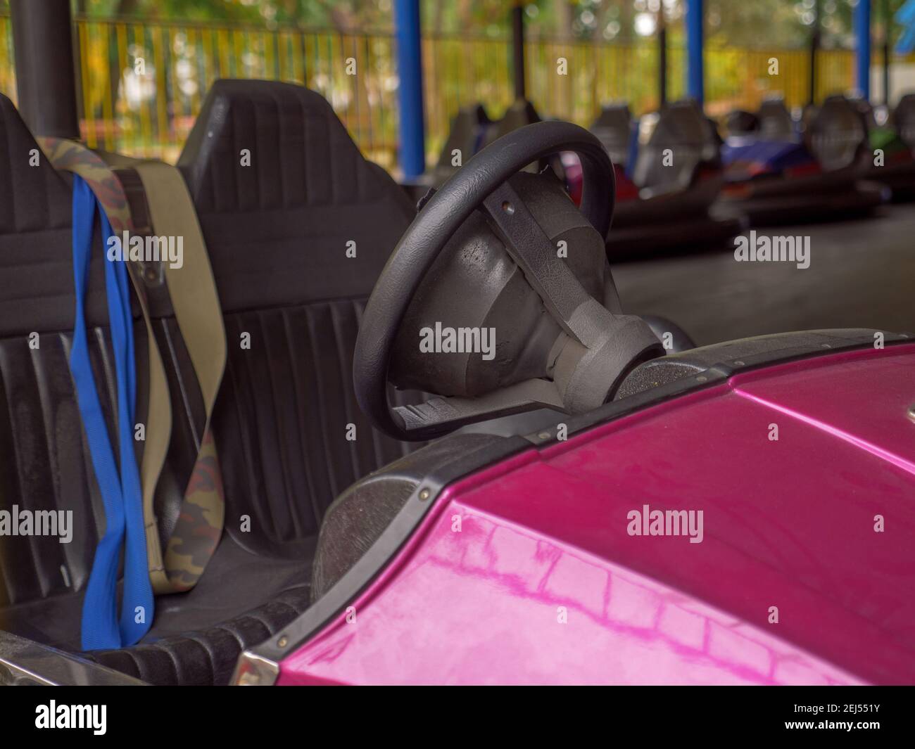 Closeup of a wheel and two seats of an electric old-fashioned bumper car and a row of autos standing behind in a city amusement park. Family fun. Stock Photo