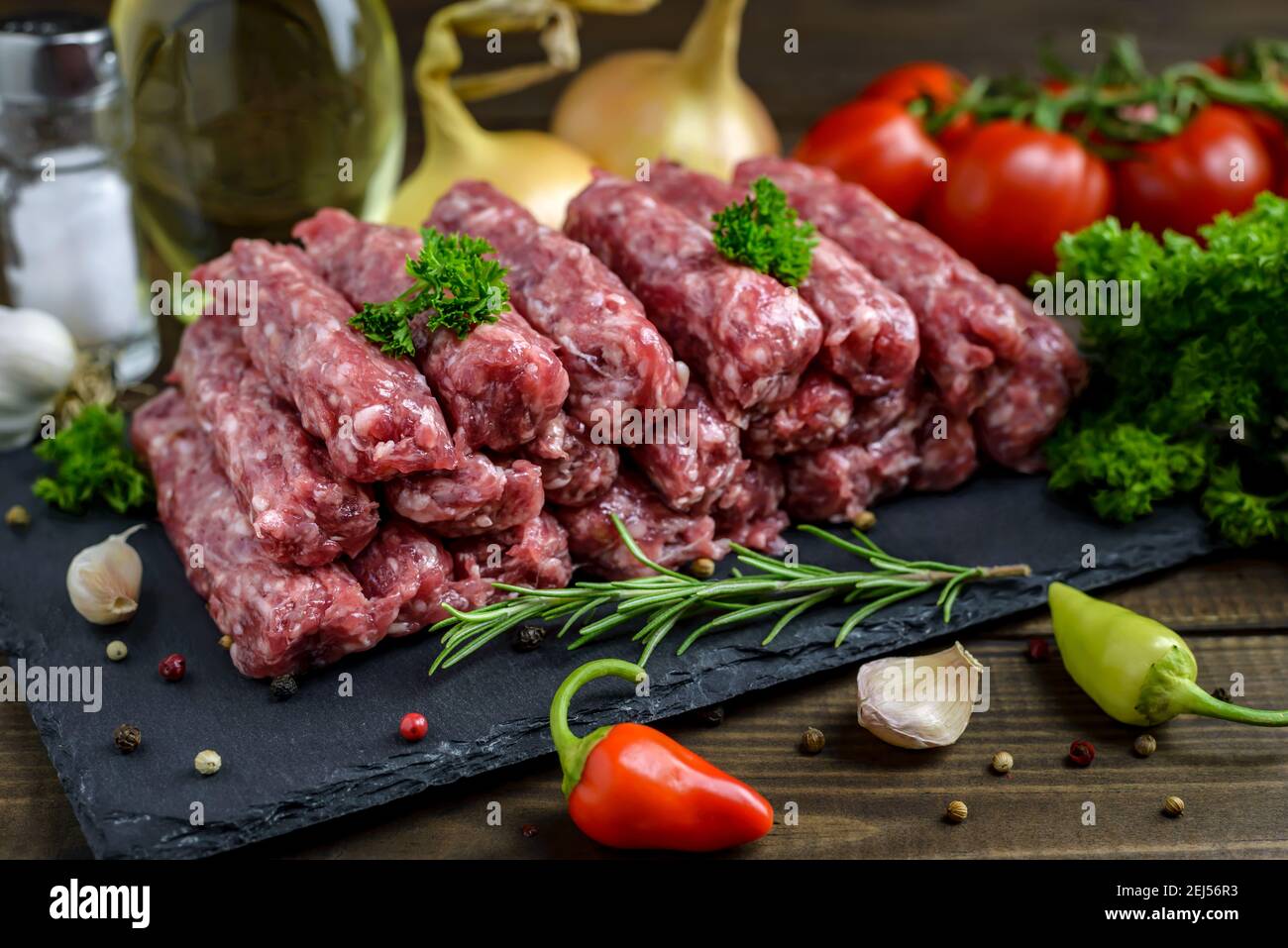 Raw minced meat cevapi ready for barbeque with various fresh vegetables on a wooden table. Selective focus. Stock Photo