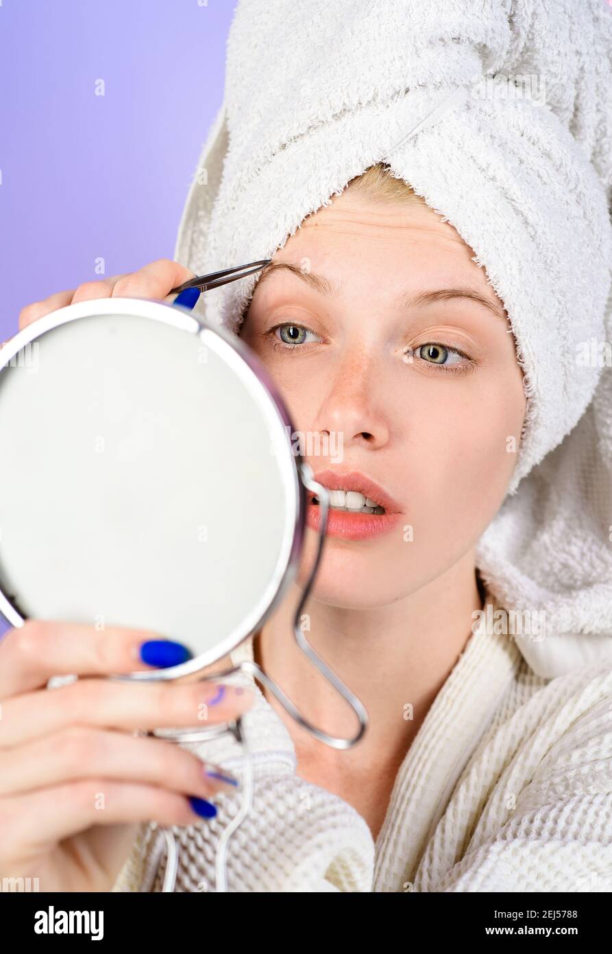 Epilate eyebrows. Girl pluck eye brow looking in mirror. Woman with tweezers. Beauty care. Correction procedure in beauty salon. Stock Photo