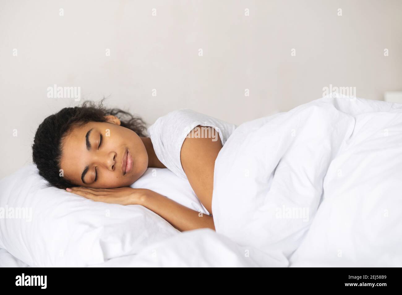 Peaceful girl sleeping well in cozy pure bed in the hotel on soft fresh pillow white linen mattress, enjoy sleep, side view, watching the dreams Stock Photo
