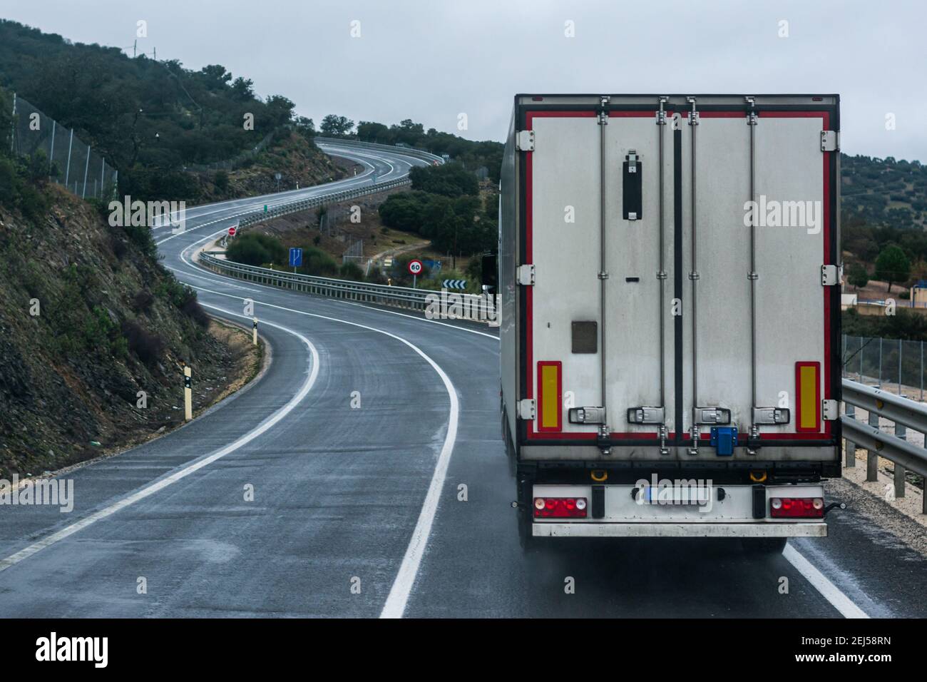 Refrigerated truck driving on a conventional road, with a continuous line and many curves. Stock Photo