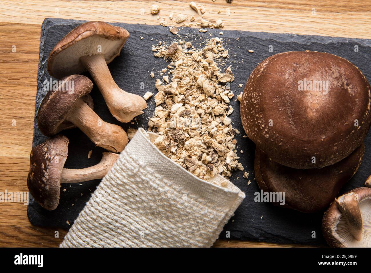 Flat lay view of dry powder made of shiitake mushrooms, Lentinula edodes. Food ingredient on black stone cutting board with fresh shiitake mushrooms Stock Photo