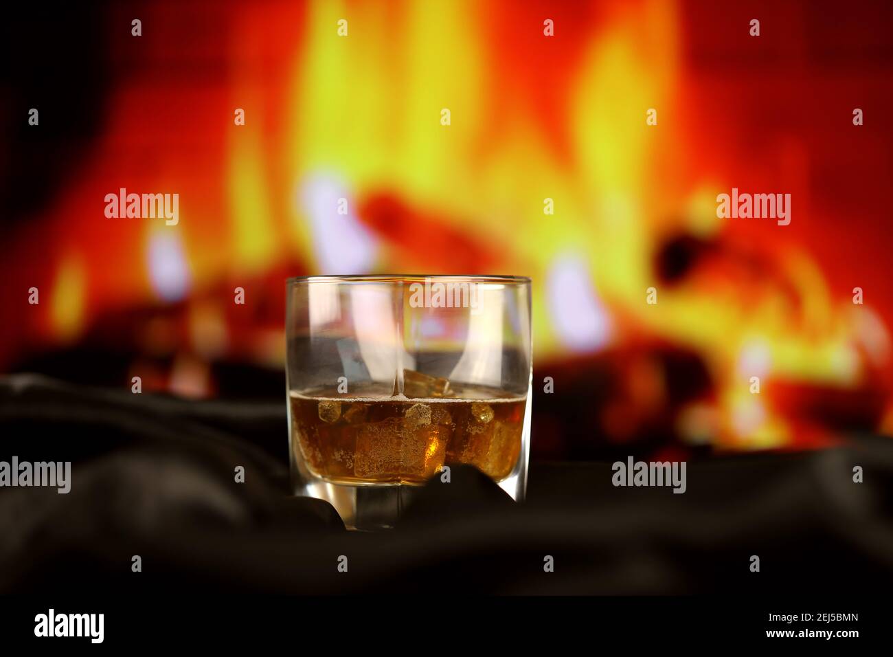 Whisky or whiskey or bourbon with ice on wooden surface on fireplace background. Luxury elite alcohol in wide glass. Low key dark scene Stock Photo