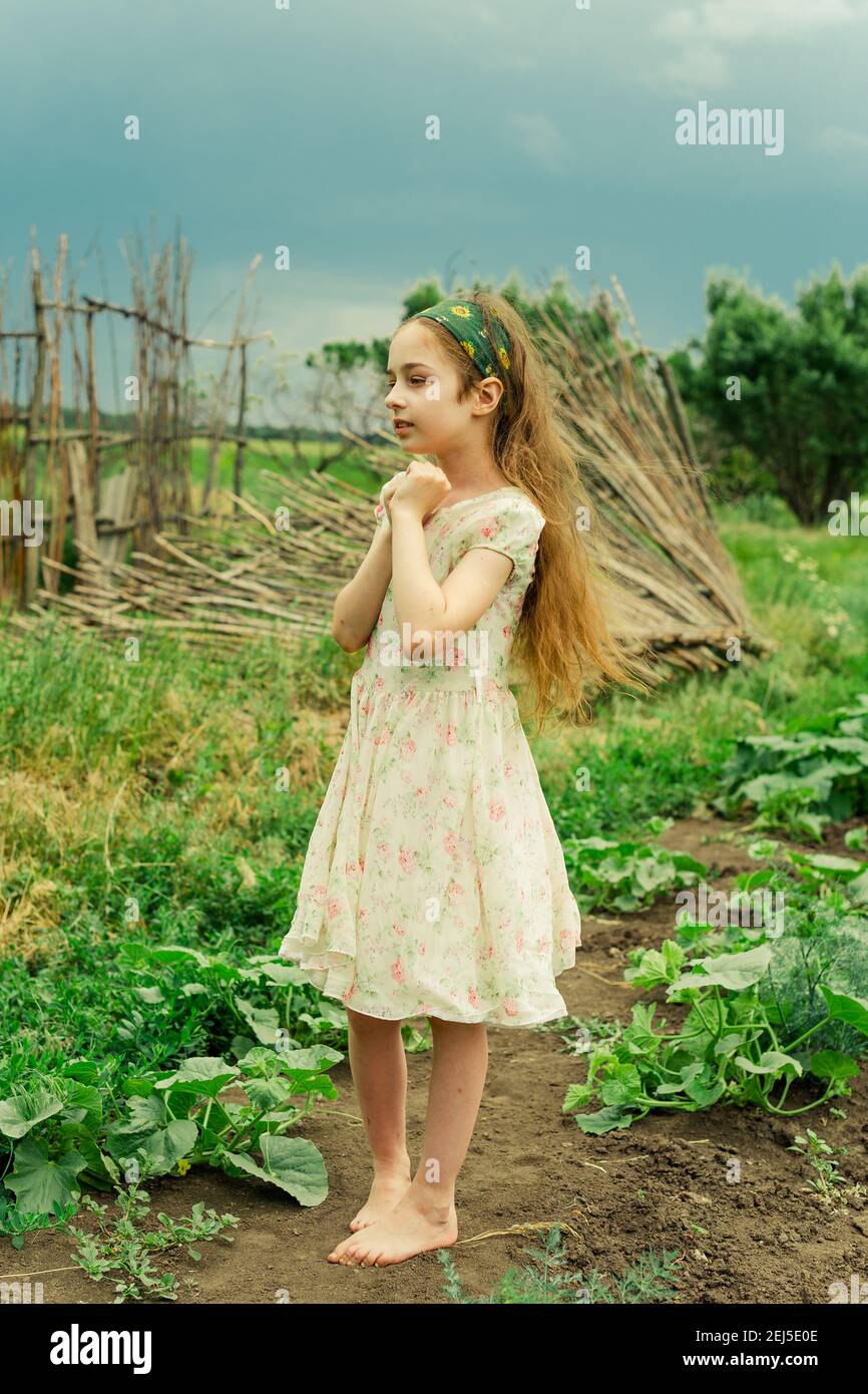 A little girl in a white dress with a flower stands barefoot in the ...