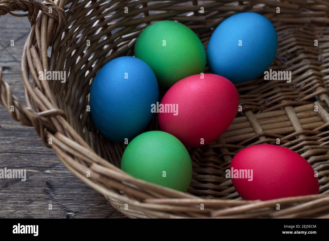 Colored easter eggs in a wicker basket on a wooden surface Stock Photo