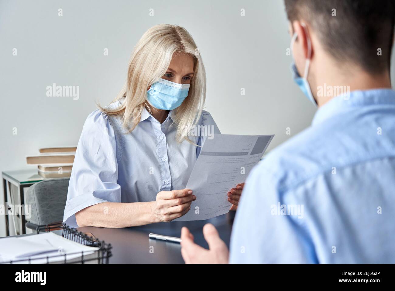 Female hr manager, employer wearing face mask reading cv at job interview. Stock Photo
