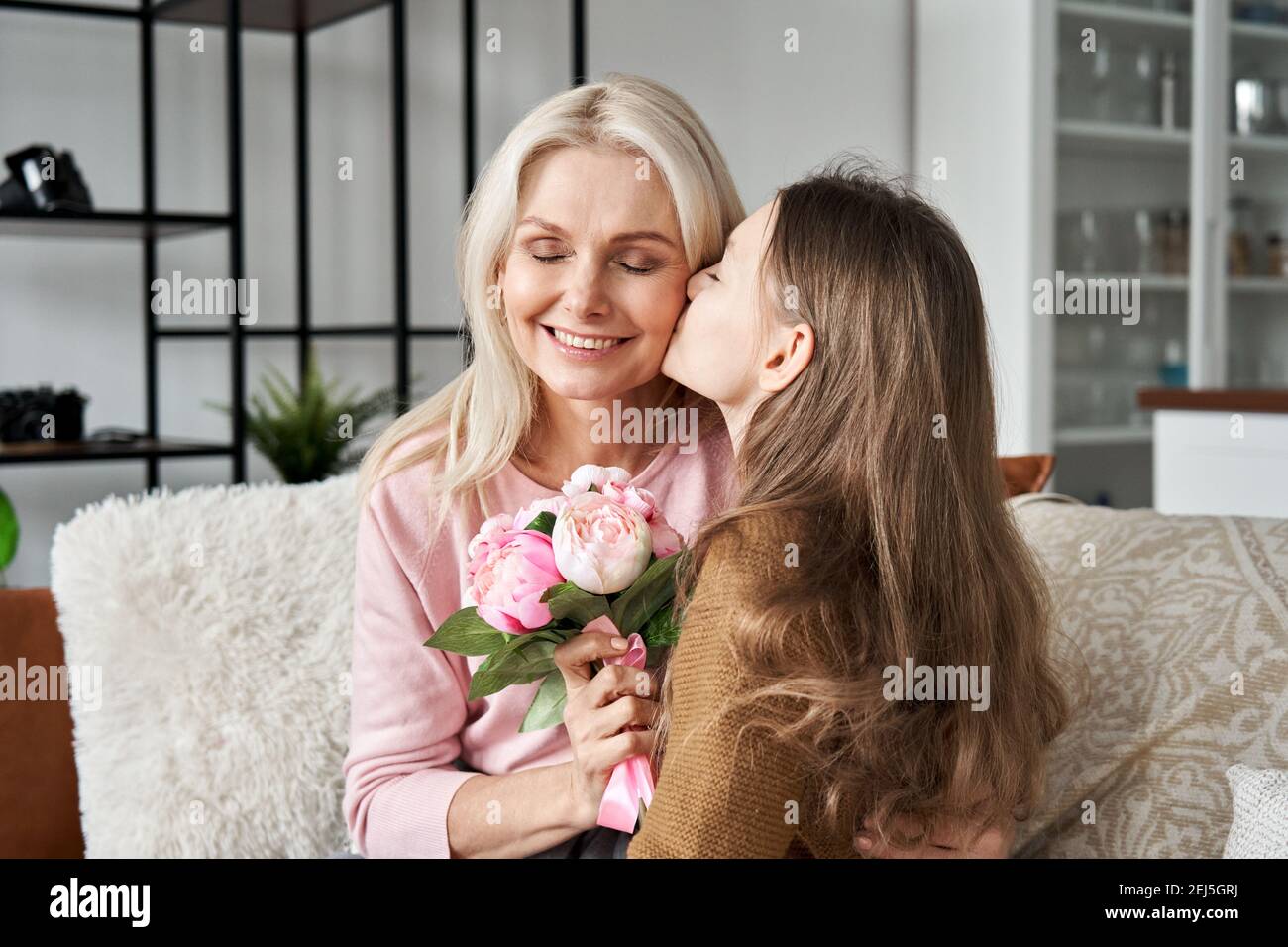 Cute teen child daughter presenting spring flowers kissing mom on Mothers Day. Stock Photo