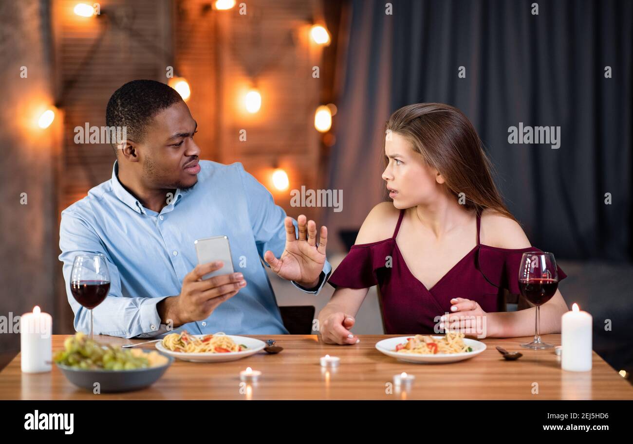 Annoyed Woman Arguing With Boyfriend In Restaurant, Blaming Him For Smartphone Addiction Stock Photo