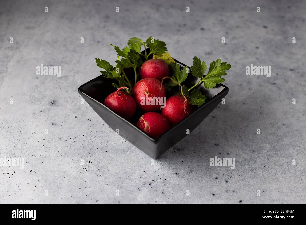 Black bowl of radishes sitting on a cork pad and concrete surface Stock Photo