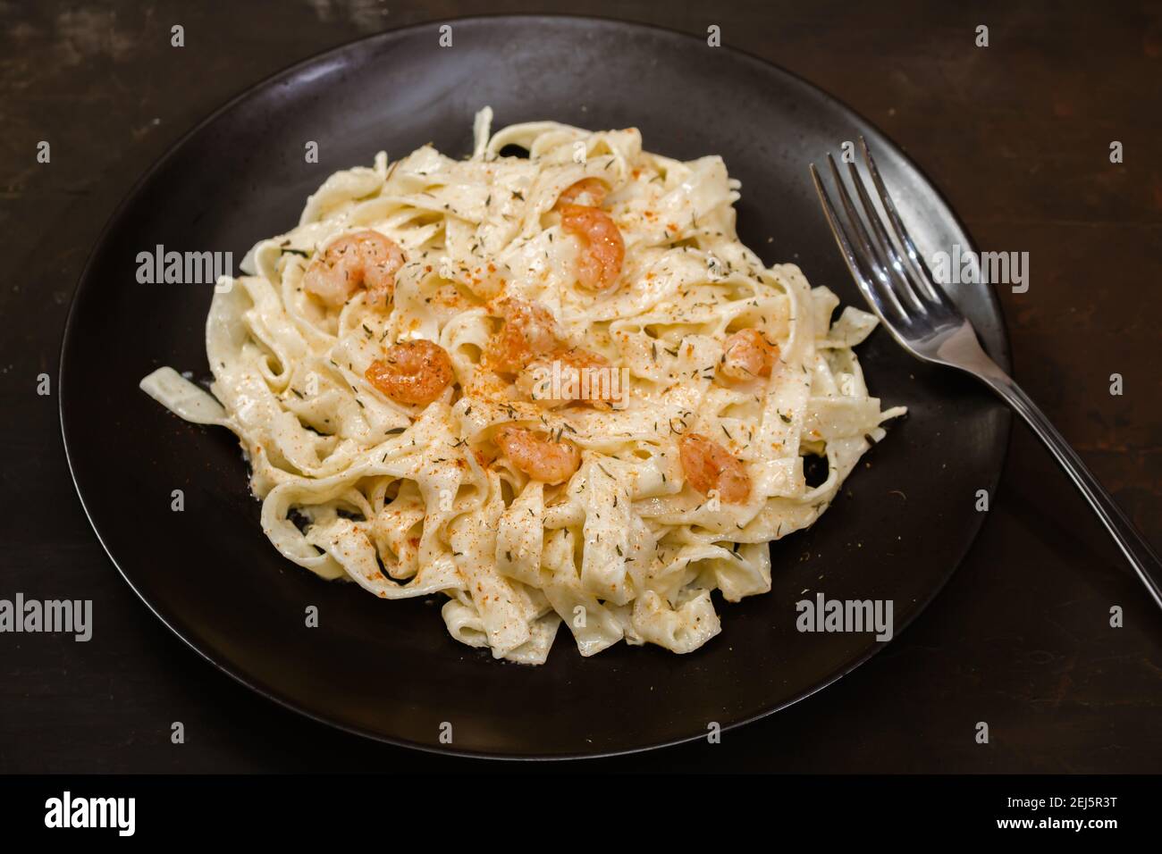 Delicious Italian pasta. Fetuccini with shrimp and herb sauce on black plate. Stock Photo