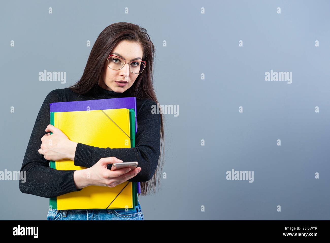 woman with smartphone holding a colorfuls folders with documents, isolated on dark background Stock Photo