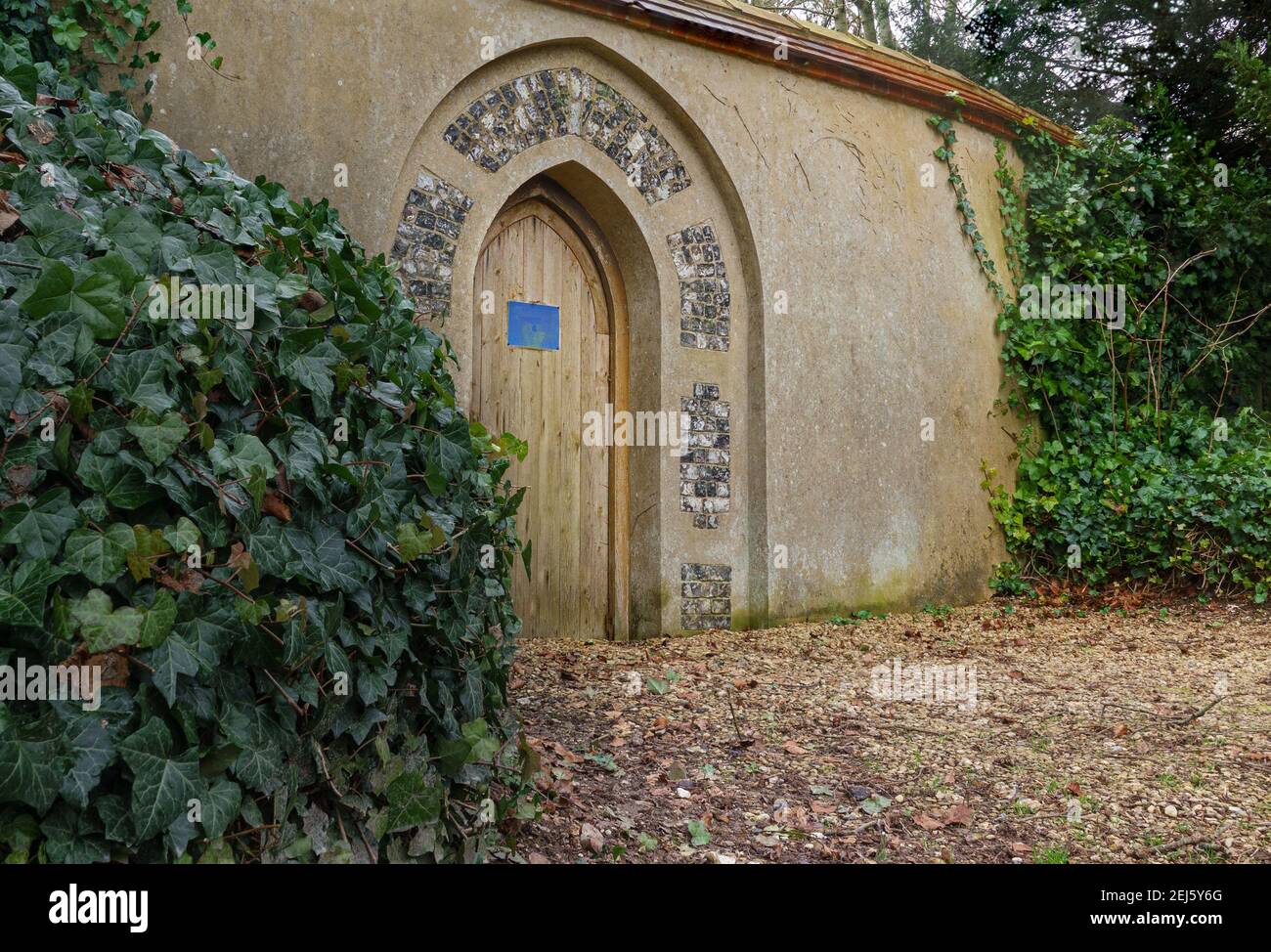 wooden cathedral arch door in a rendered stone wall leading to the vicarage garden Stock Photo