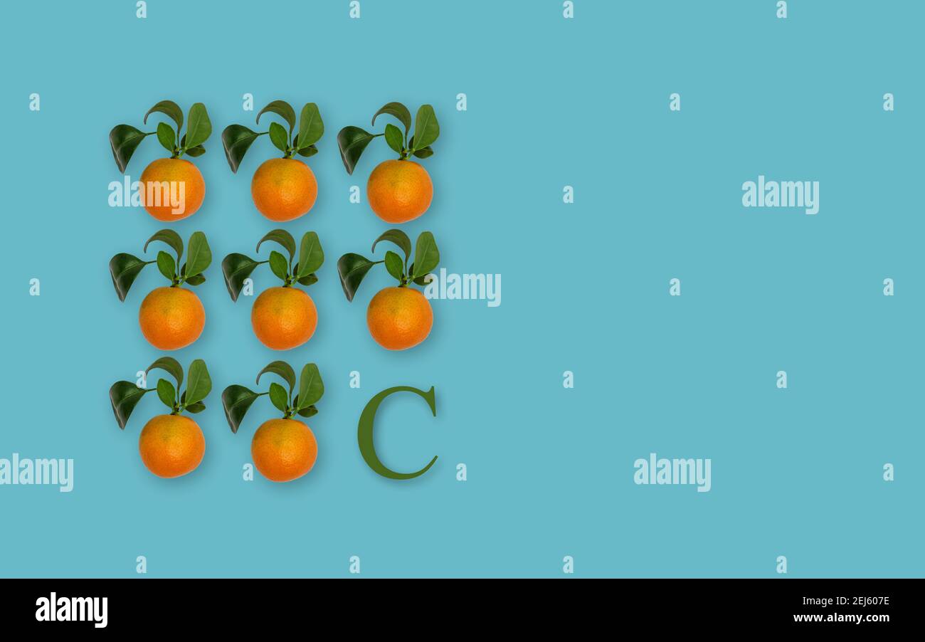 Eight ripe orange clementines and green letter C vitamin C on blue background. Copy space
