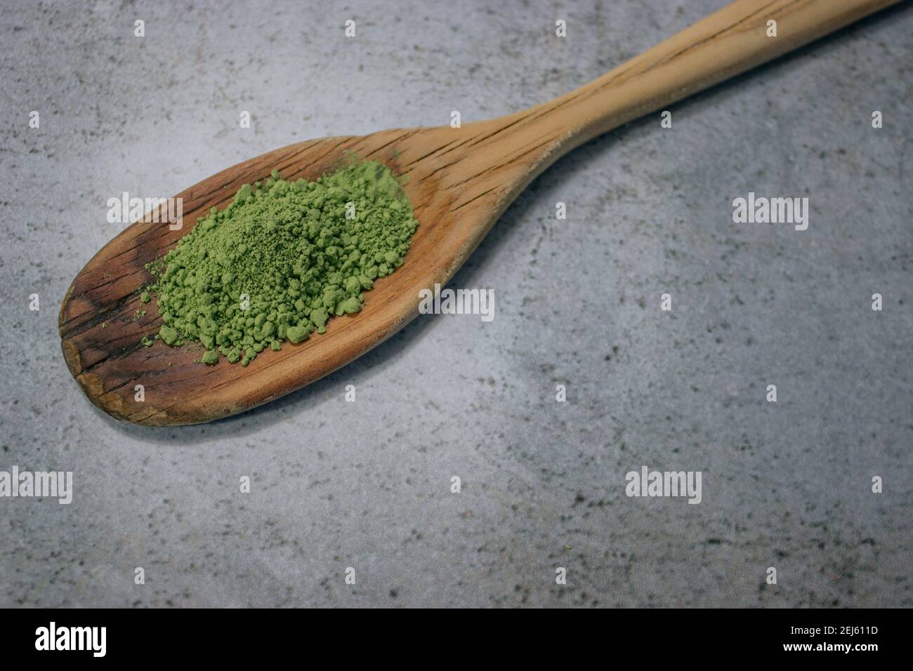 Close up matcha tea powder on wooden spoon on Gray Stone Background