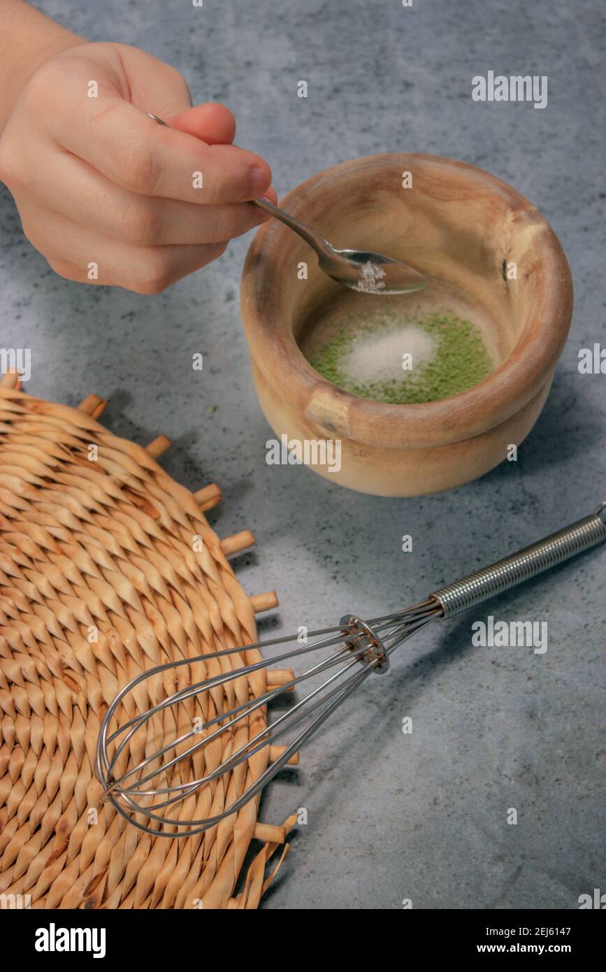 Vertical image of matcha tea powder  and spoon pouring sugar into the clay bowl on Gray Stone Background. Japanese Matcha Tea Preparation 2021. Stock Photo