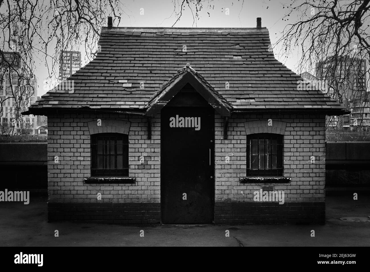 Black and white monochrome image of a small 1 story brick building with one black door, two windows and slate roof. Stock Photo