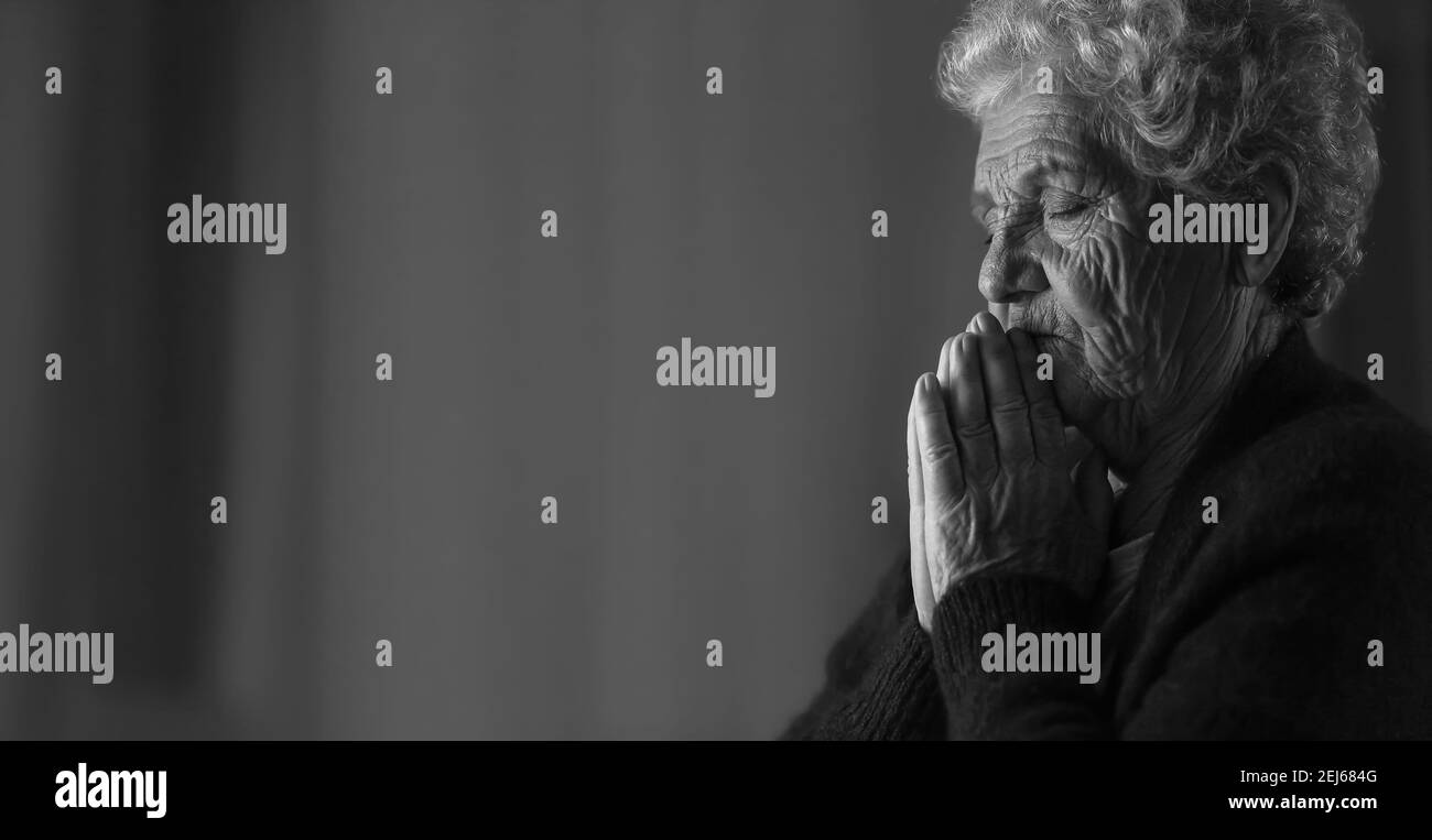 Black and white portrait of senior woman praying to God on dark background Stock Photo