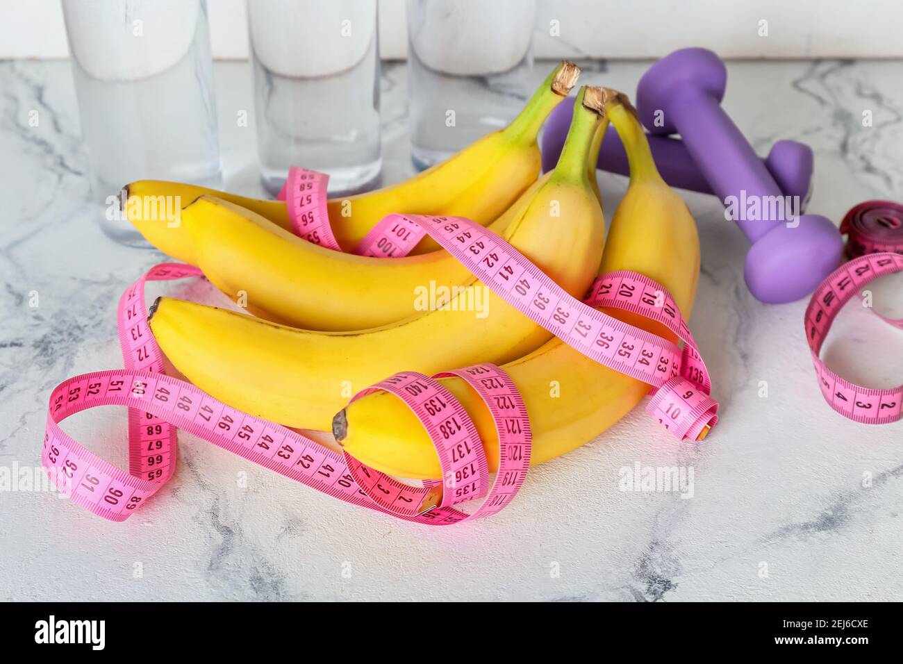 Ripe bananas, measuring tape and dumbbells on light background. Weight