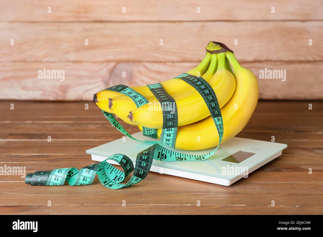 Ripe bananas, measuring tape and scales on wooden background. Weight