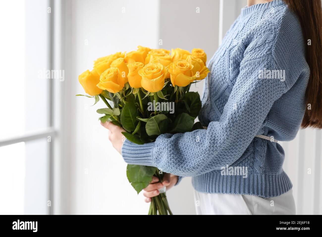 Young woman with beautiful yellow roses in room Stock Photo - Alamy