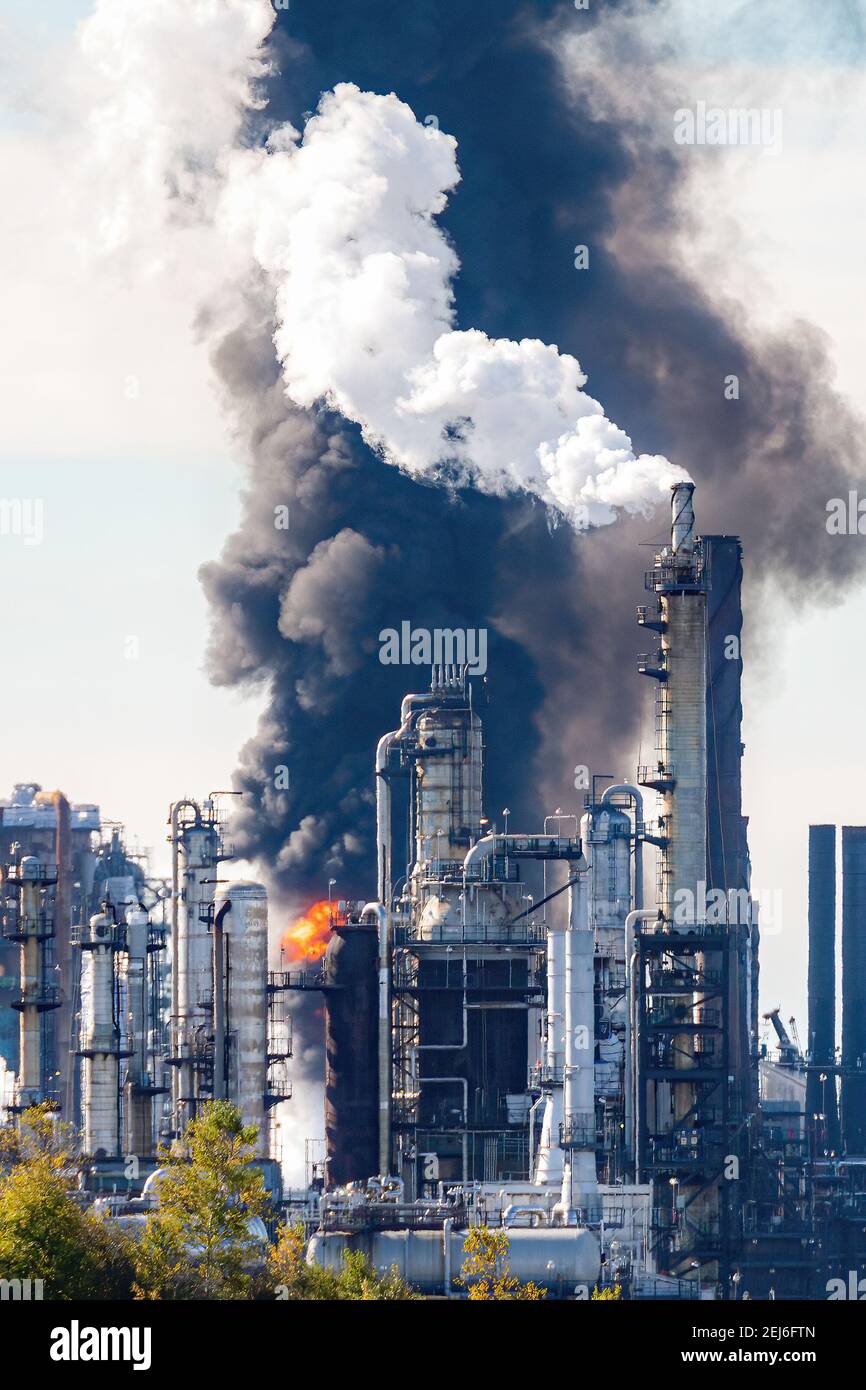 Fire and black smoke at an oil refinery after an explosion. Towers visible in front of smoke and flame. Scene slightly blurred due to volatile air. Stock Photo