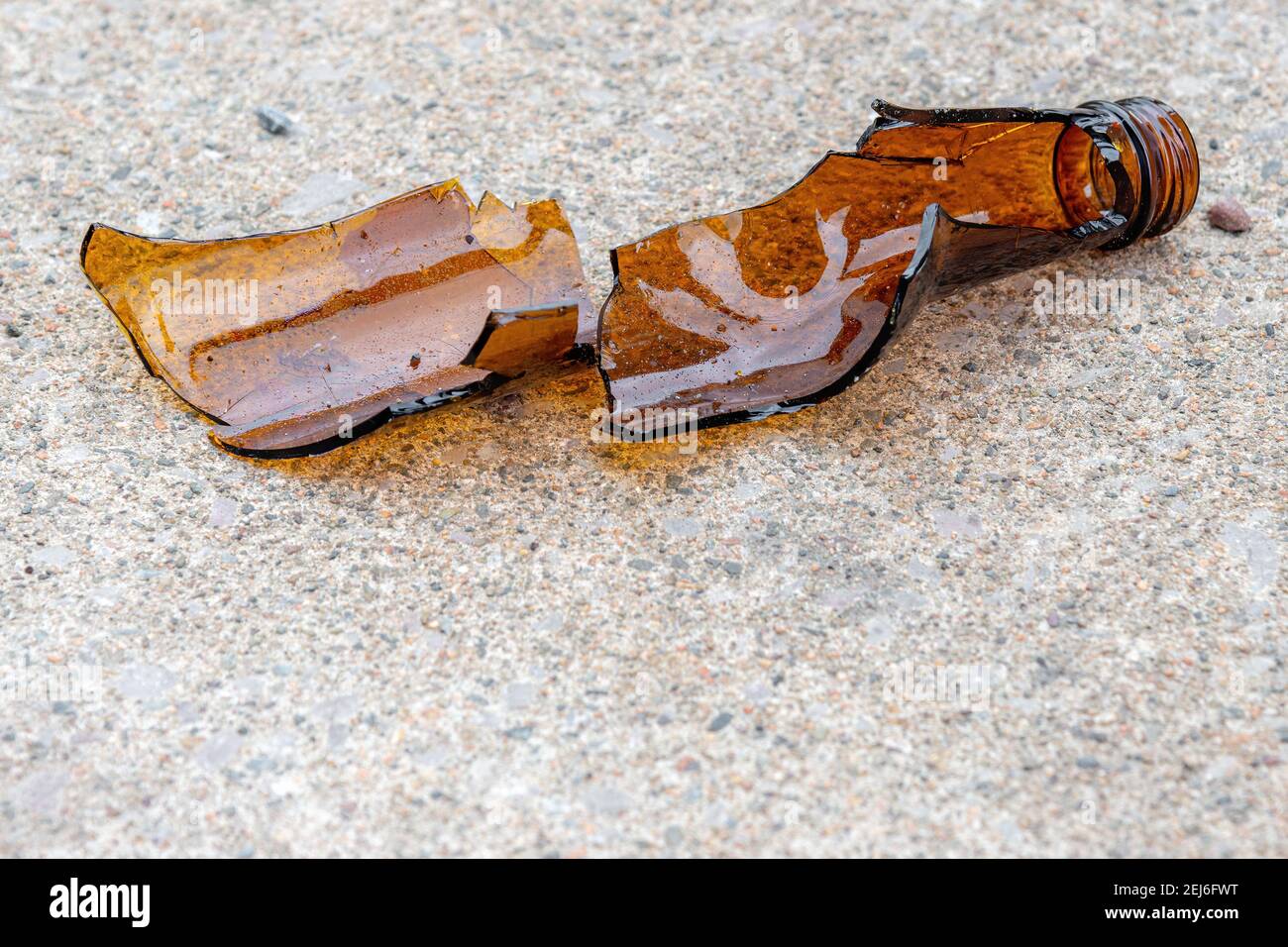 A brown broken beer bottle on a concrete sidewalk. Only part of the