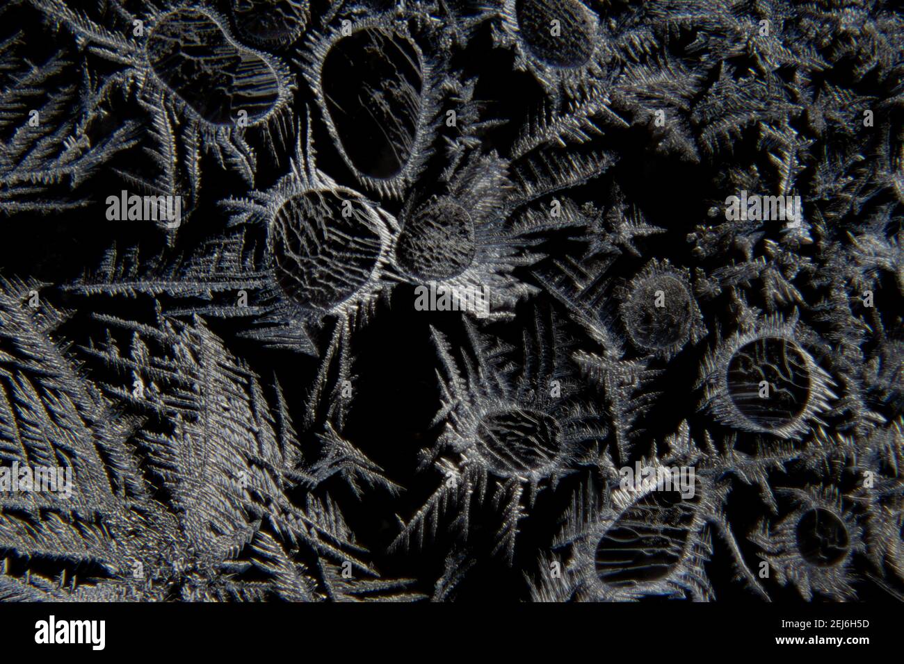 Macro of abstract shapes of ice crystals and frost flowers on a glass window with black background Stock Photo