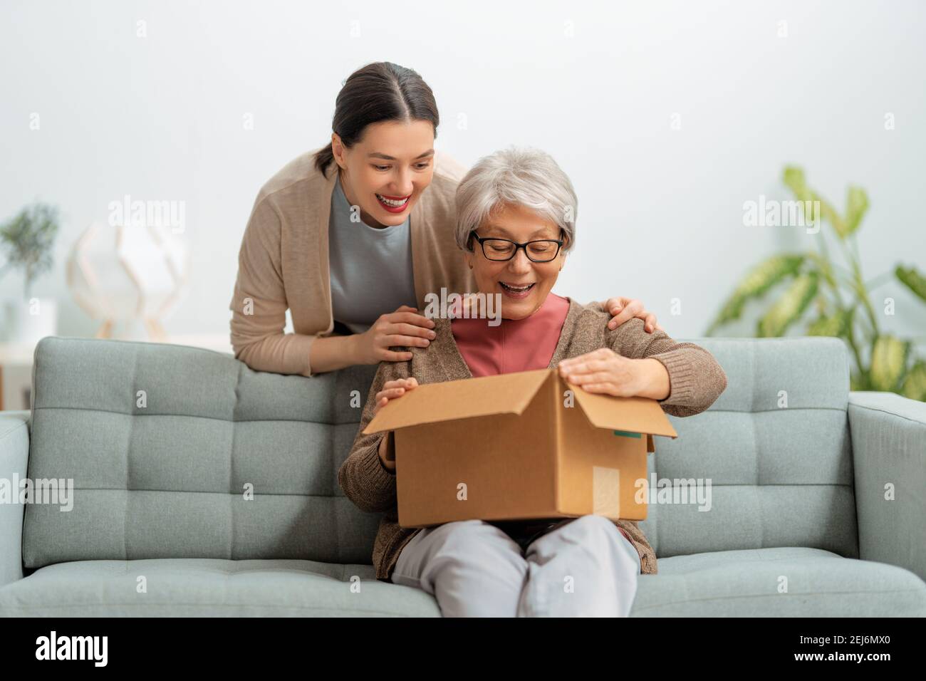 Two women are holding cardboard box sitting on sofa at home Stock Photo ...