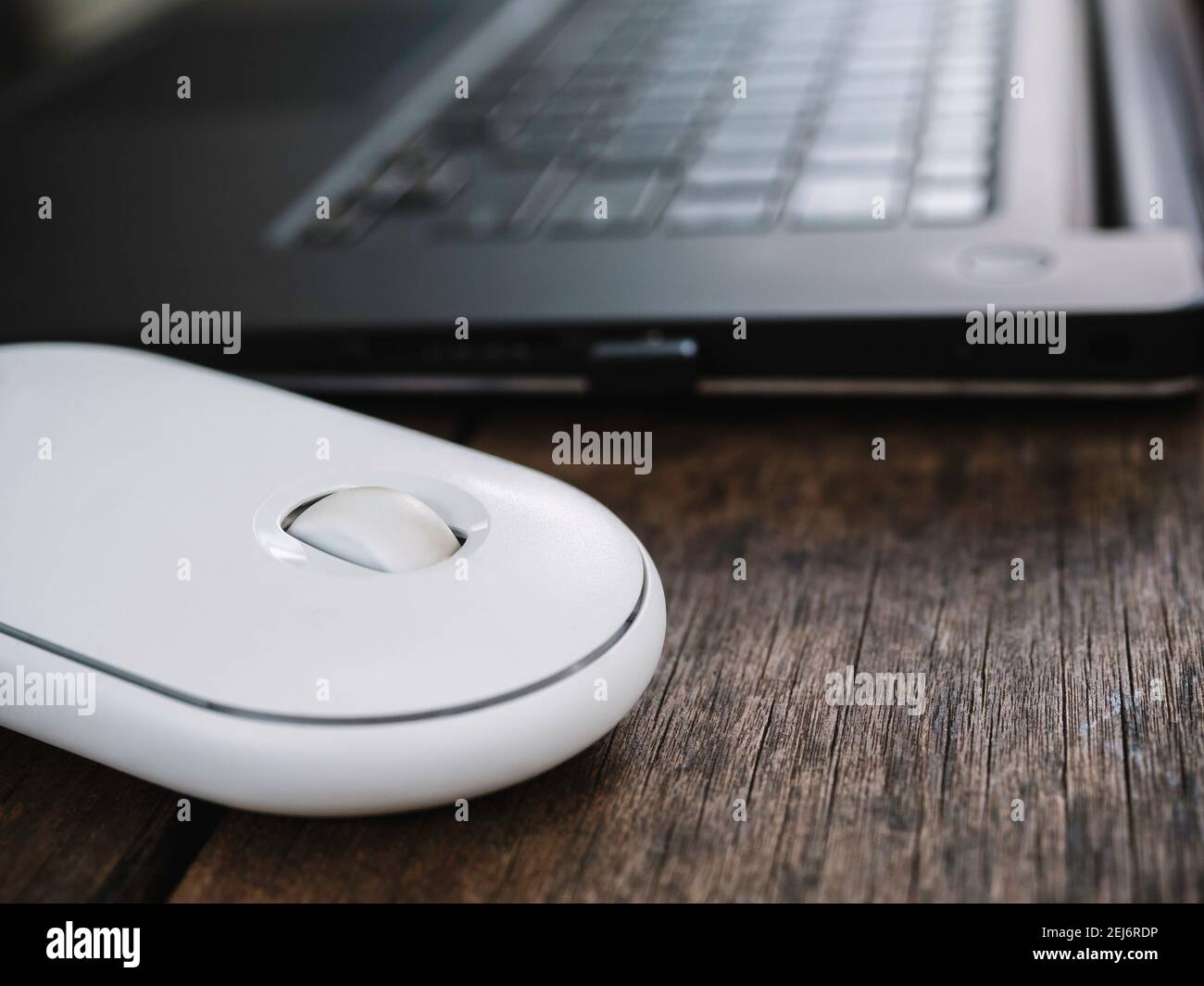 Close up modern white wireless mouse beside black laptop computer on wooden desk. Stock Photo