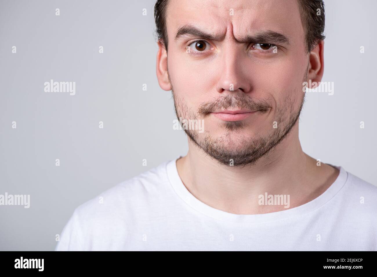 Handsome brunette guy with bristles in a white T-shirt makes funny grimaces  on his face Stock Photo - Alamy