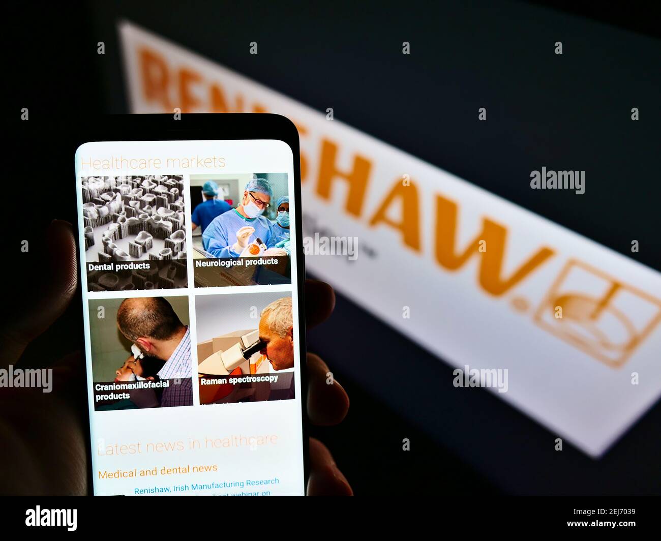 Person holding cellphone with logo of British engineering company Renishaw plc on screen in front of web page. Focus on center of phone display. Stock Photo