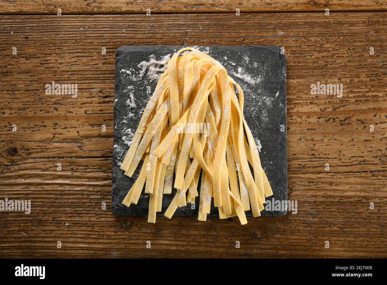 Freshly prepared handmade bundle of Fettuccine Italian pasta ribbons sprinkled with flour for advertising, food or recipe themes on a small board on w Stock Photo