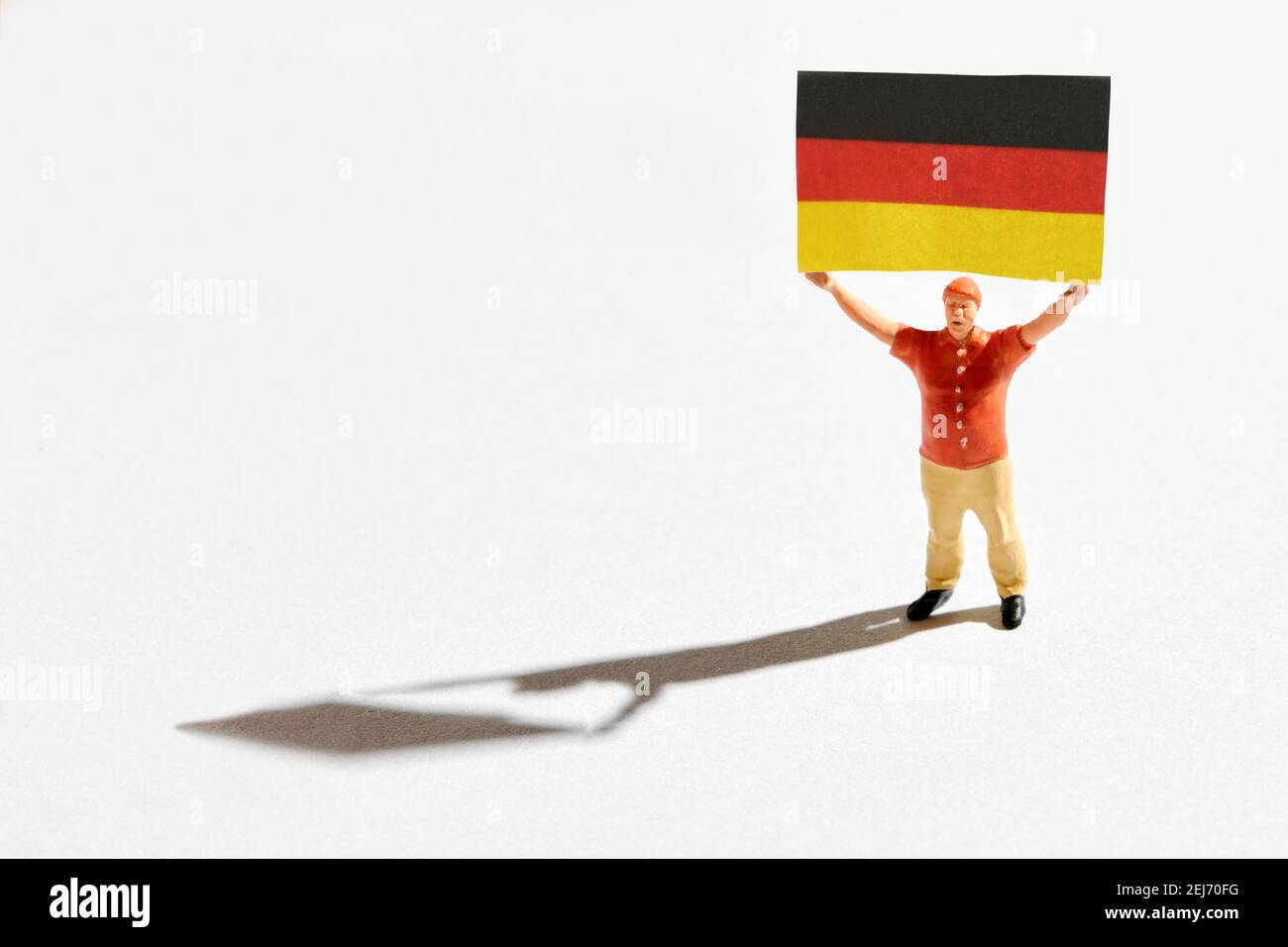 Miniature male patriot holding German flag in raised arms during demonstration against gray background Stock Photo