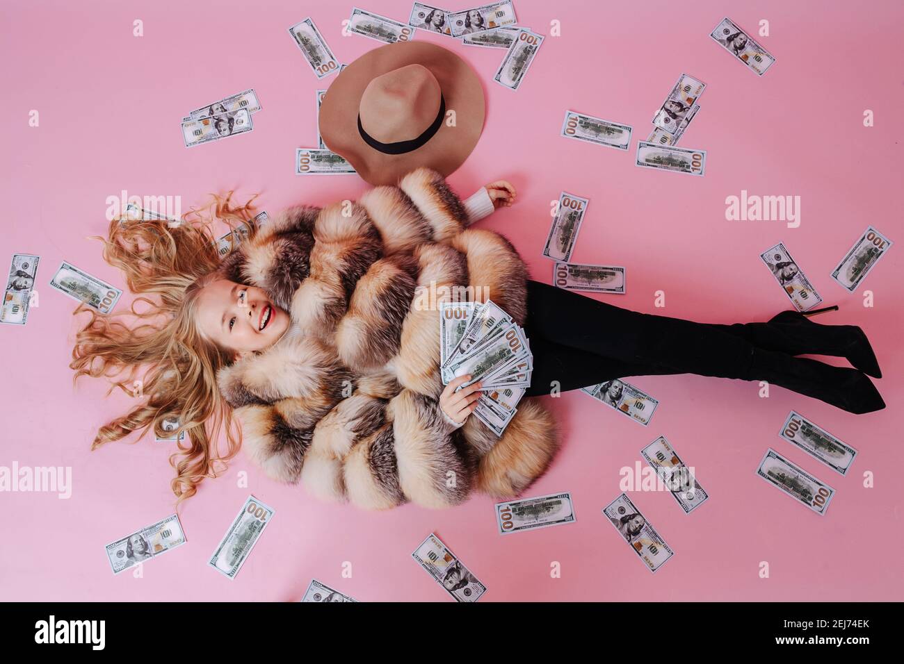 Widely smiling preteen girl in oversized luxurious fur coat enjoying money rain Stock Photo