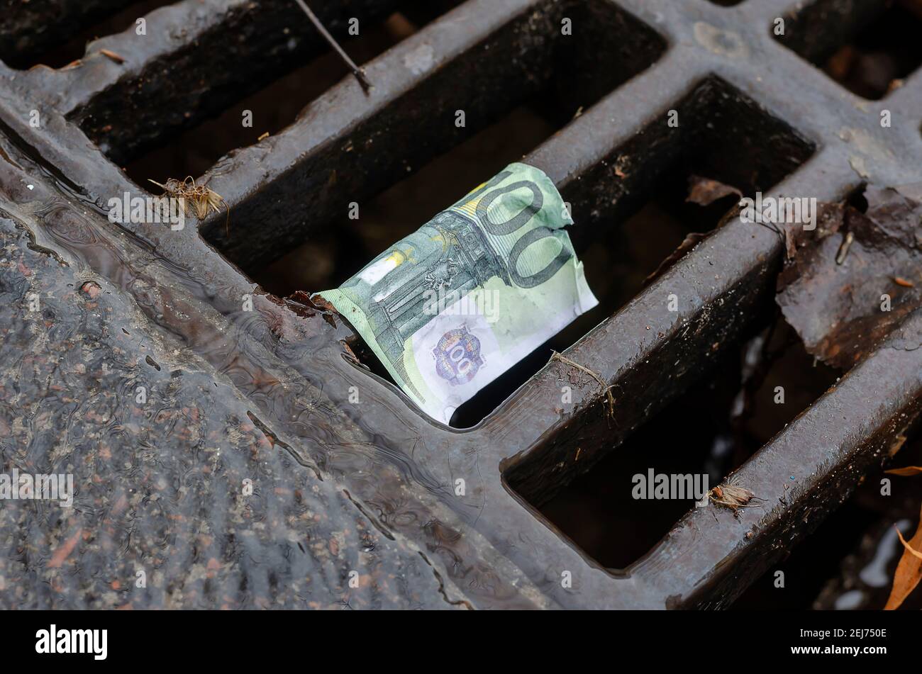 One hundred euro bill on the grate of the storm drain. Wet banknote snagged on a metal grate. Close-up. Selective focus. Stock Photo