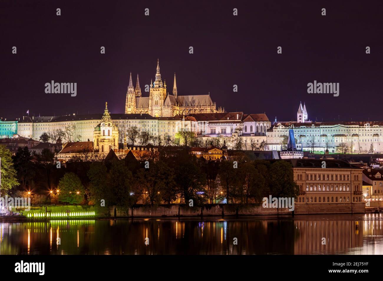 Charles Bridge in Prague in the evening with colorful lights from lanterns. In the river the reflection of the evening illuminations. Stock Photo
