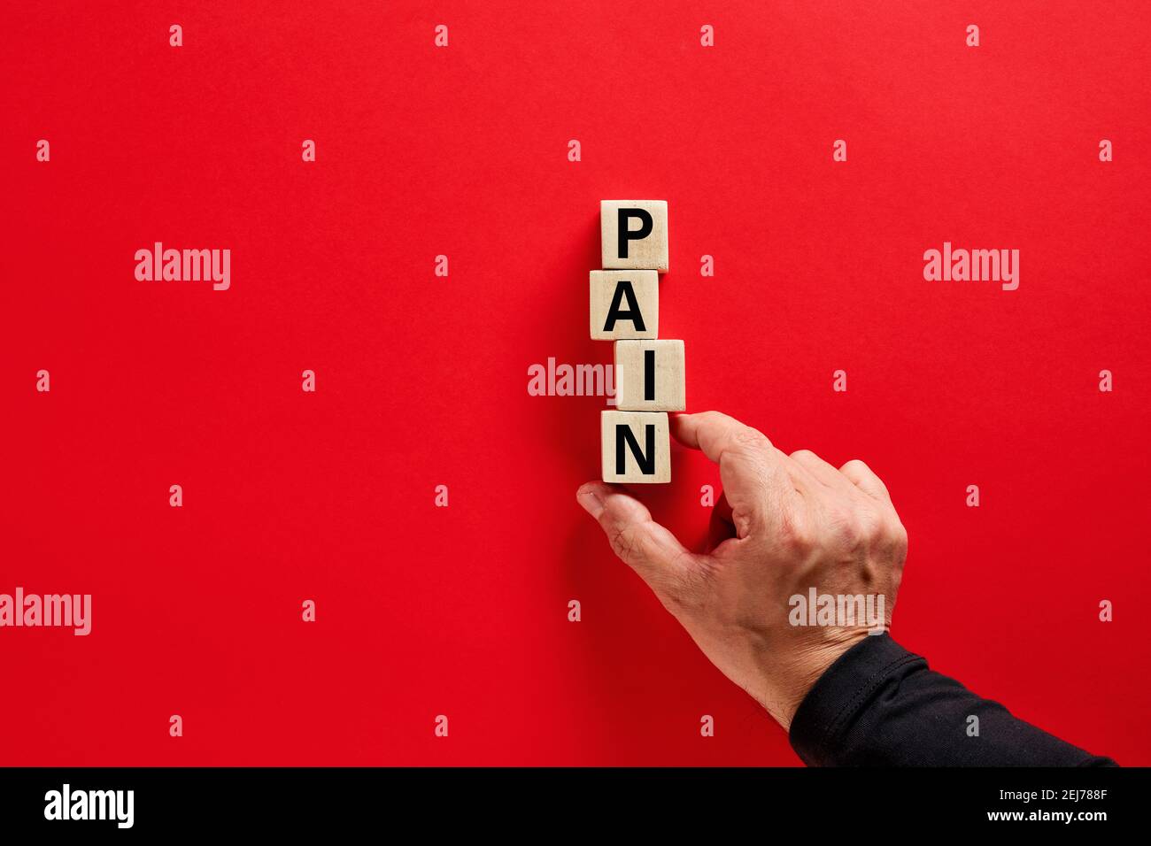 Male hand arranging the wooden blocks with the word pain on red background with copy space. Emotional, psychological or physical pain concept. Stock Photo