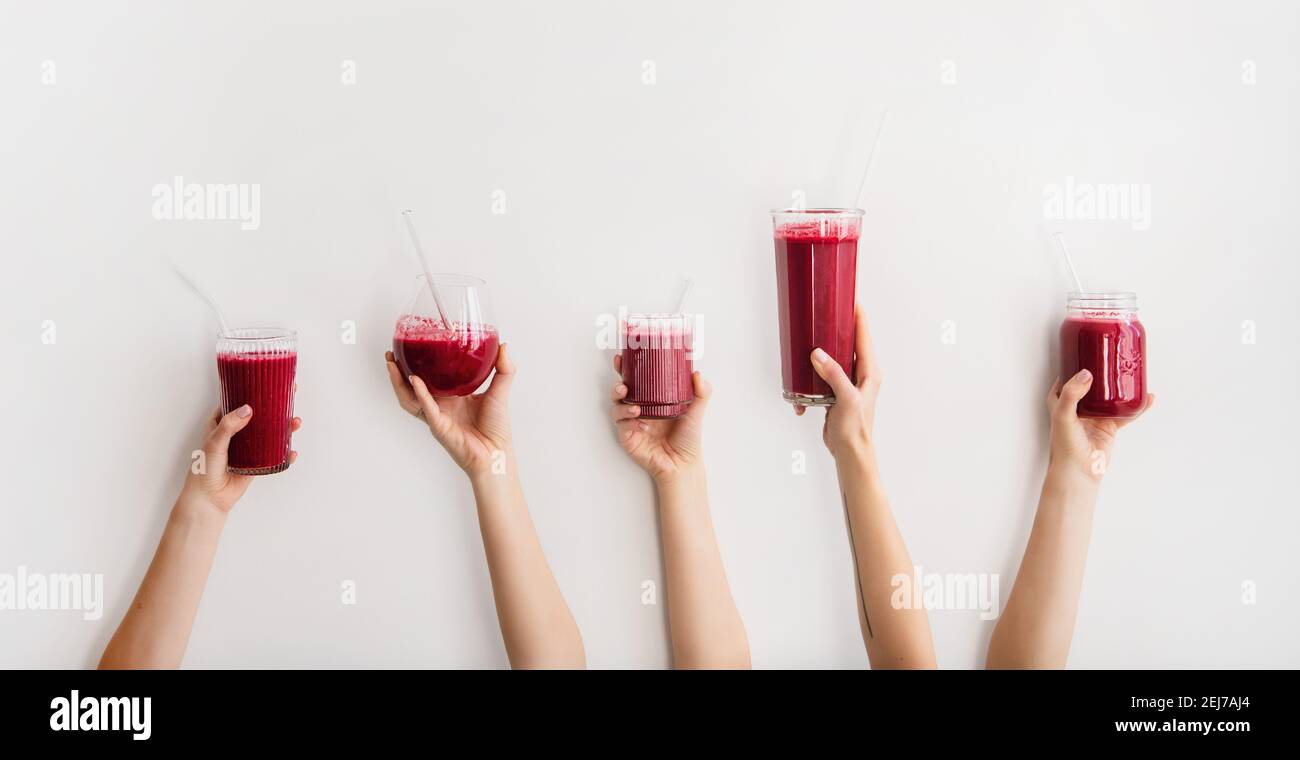 Multiple hands holding glasses with Purple beet and pomegranate fresh smoothie with glass straws, white background, copy space, wide composition. Detox, dieting, weight loss, healthy lifestyle concept Stock Photo
