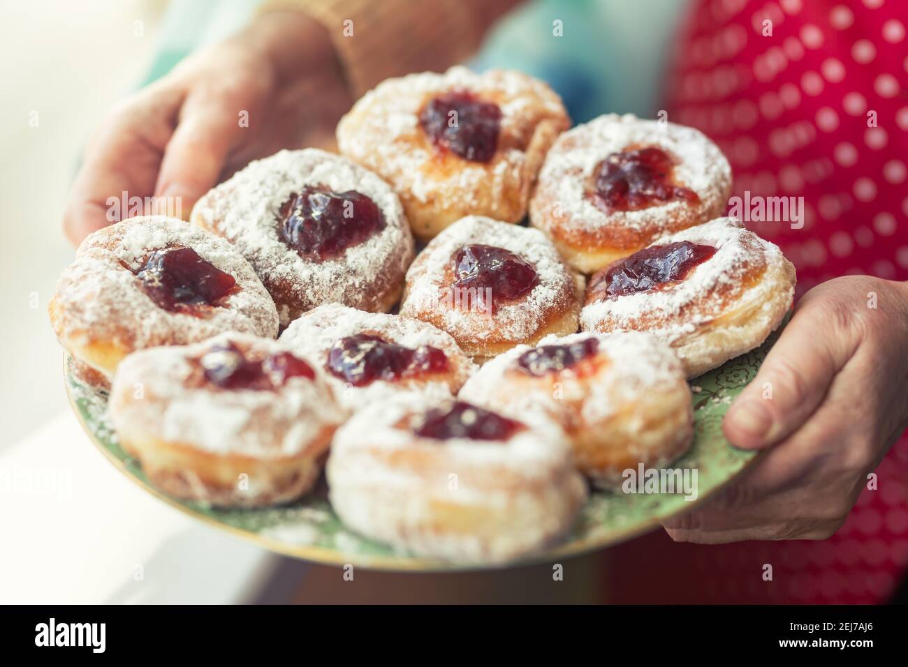 Plate full of jam-filled donuts with sugar coating held in the hands of an older woman. Stock Photo