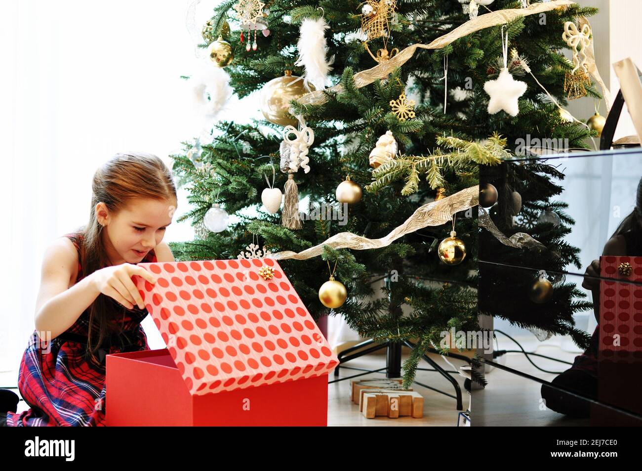 Young European girl with Christmas presents, looking in a big red box Stock Photo