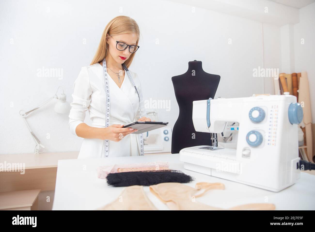 Modern fashion designer, young girl with tablet in hands next to sewing ...
