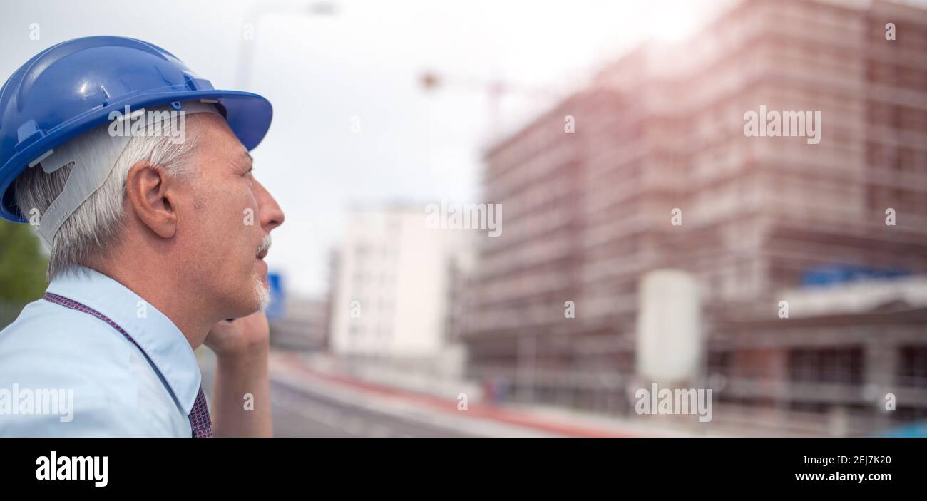 Architect talking on his mobile cellphone in front of construction site Stock Photo