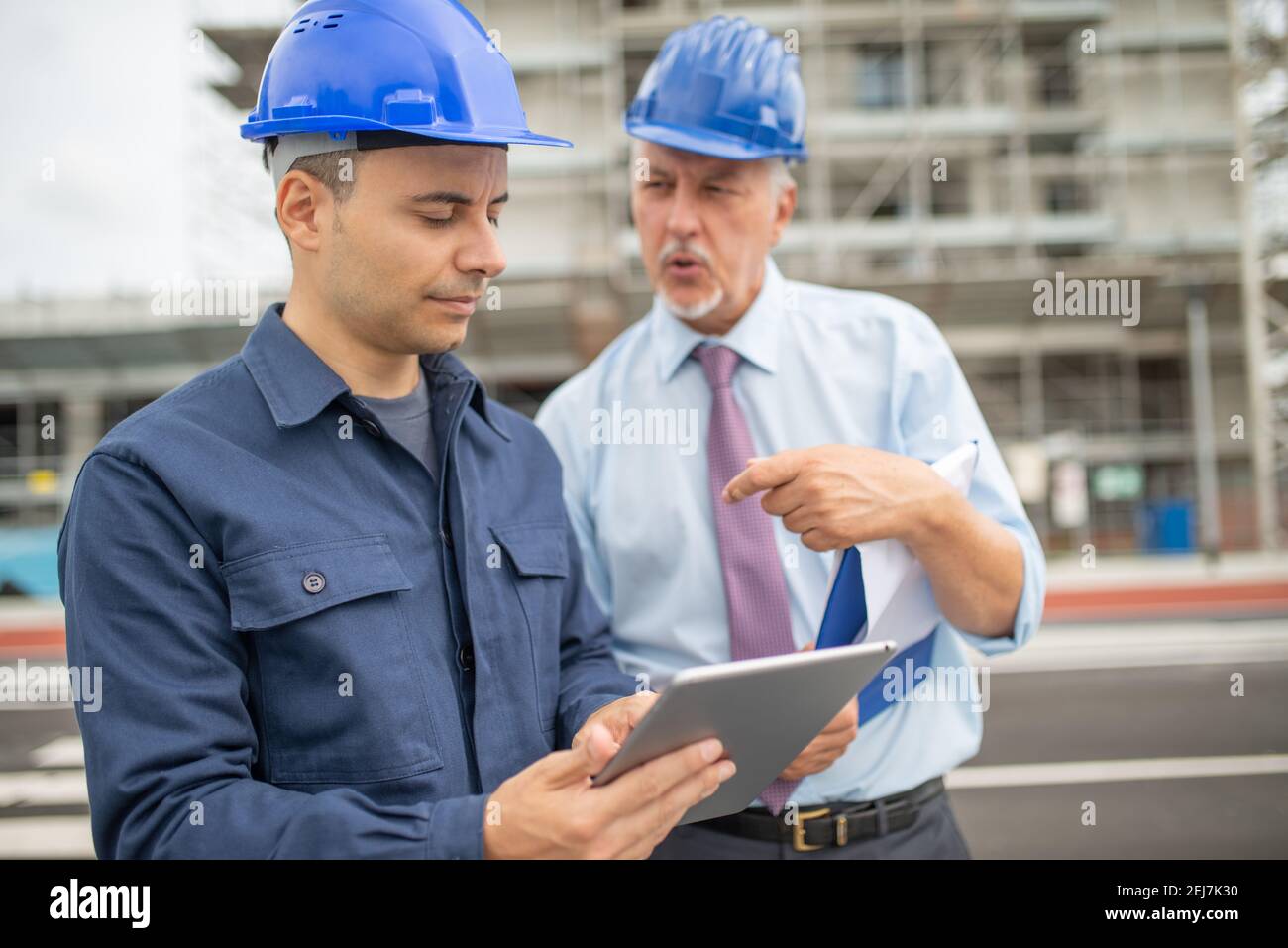 Two architect developers reviewing building plans at construction site using a tablet Stock Photo